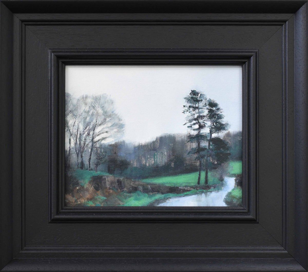 a small oil painting of pine trees in winter with green fields in a black frame