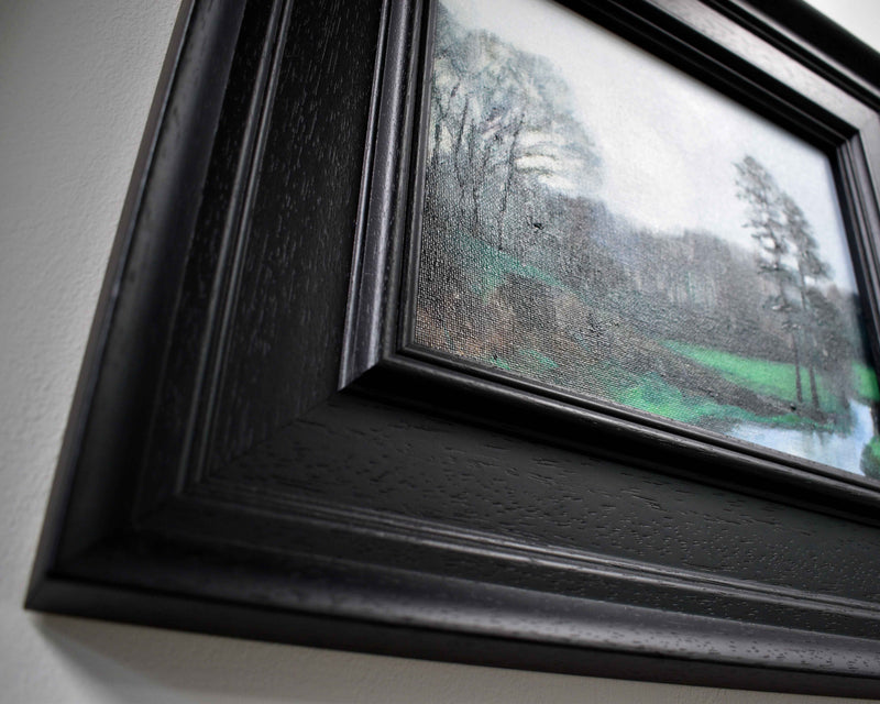 a detail picture of the corner of an ornate black frame with a small oil painting of pine trees in winter 