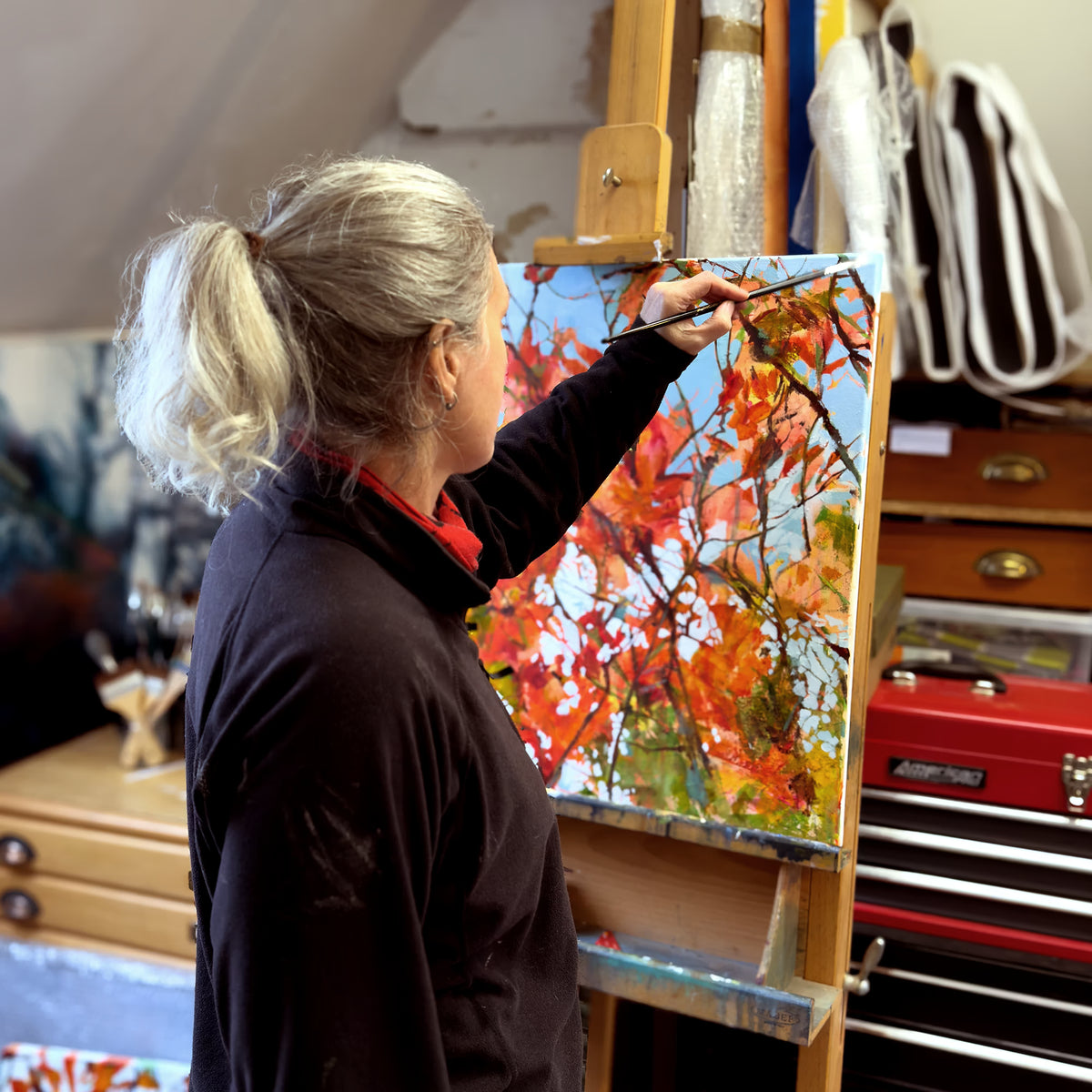 UK artist Julia Brown working on an abstract autumn painting on an easel in her Yorkshire studio.