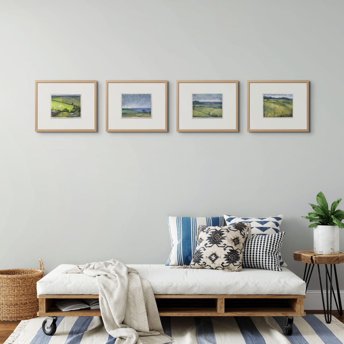 4 framed artworks of fields in a line on a wall, above a daybed dressed with cushions and blankets