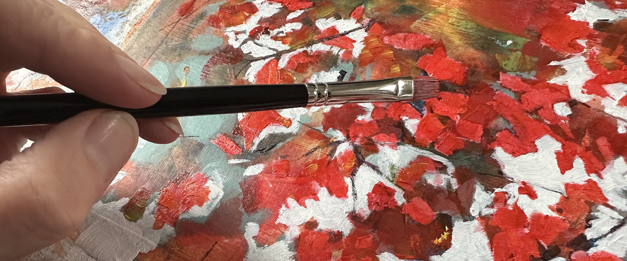a close-up of Julia Brown's hand holding a paintbrush and working on an abstract painting with red maple leaves